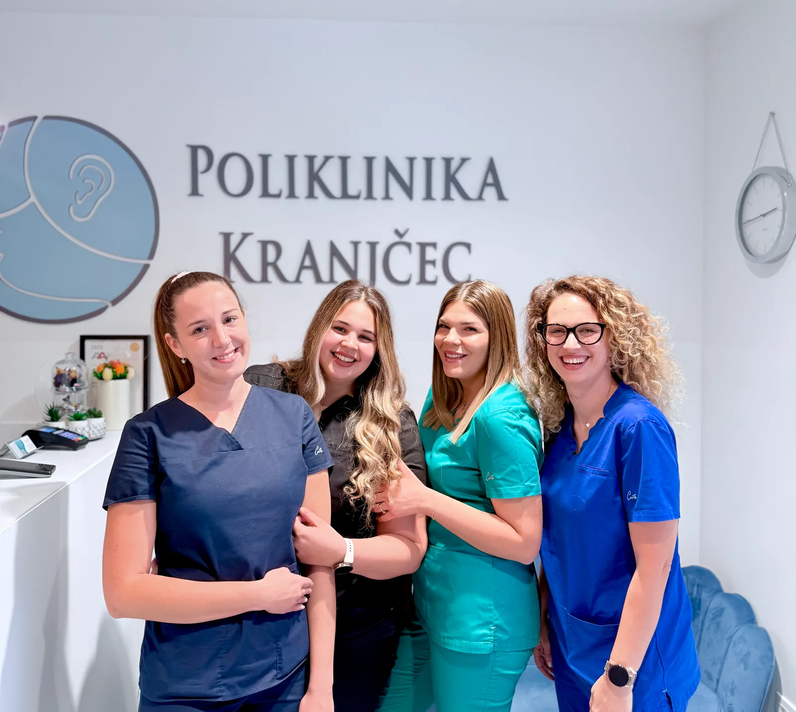 The Poliklinika Kranjčec team at the reception desk, in front of the logo